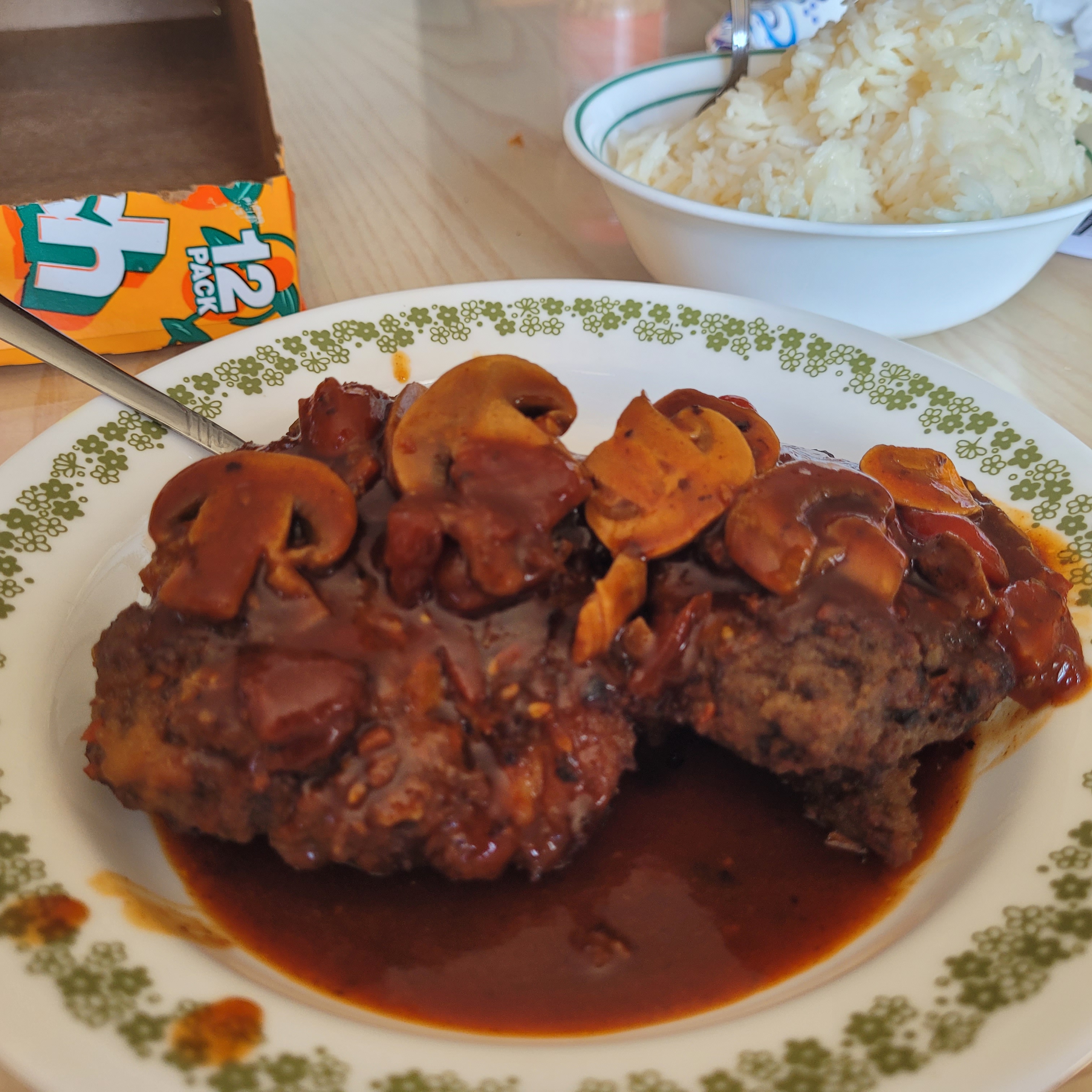 Hamburger steak with a sweet tomato sauce with a bowl of rice in the background