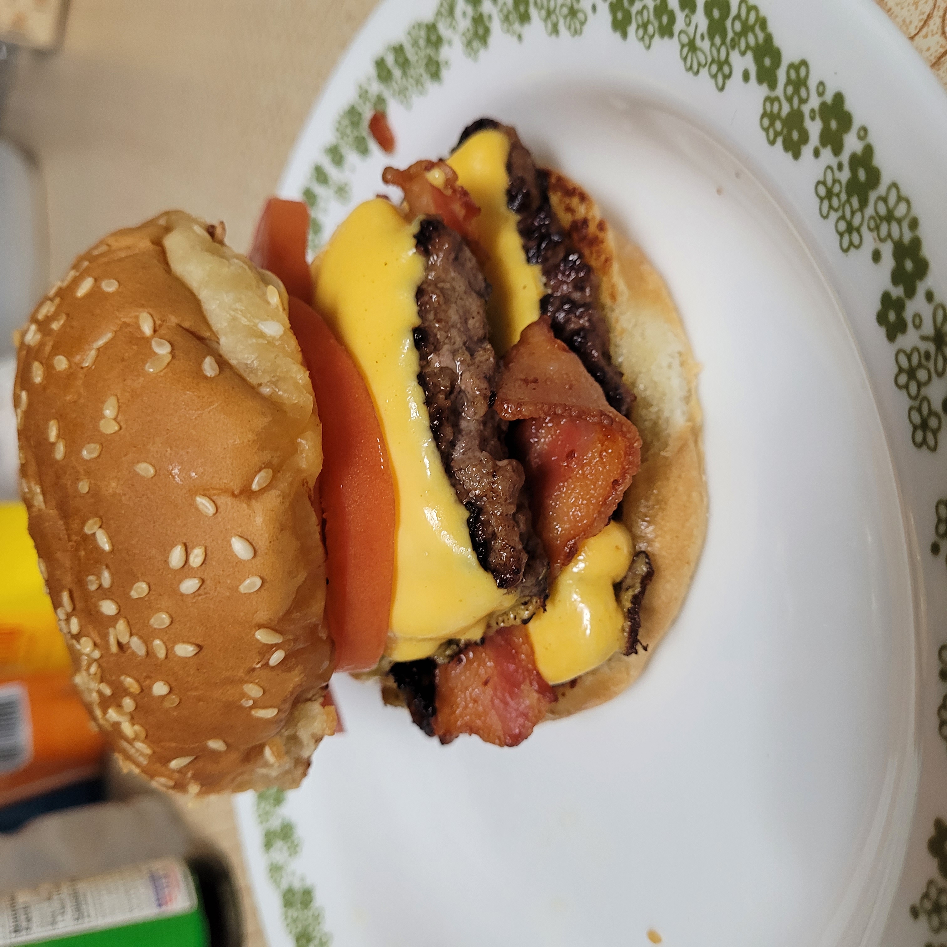 A smash burger with two paddies, bacon, and tomatoes